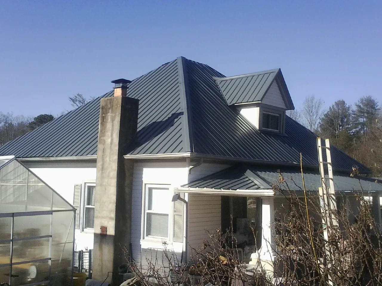 Dark blue standing seam metal roof on a white farmhouse with dormer — Slate & Tile Roof Repair by Roofing Brothers in Roxbury Crossing