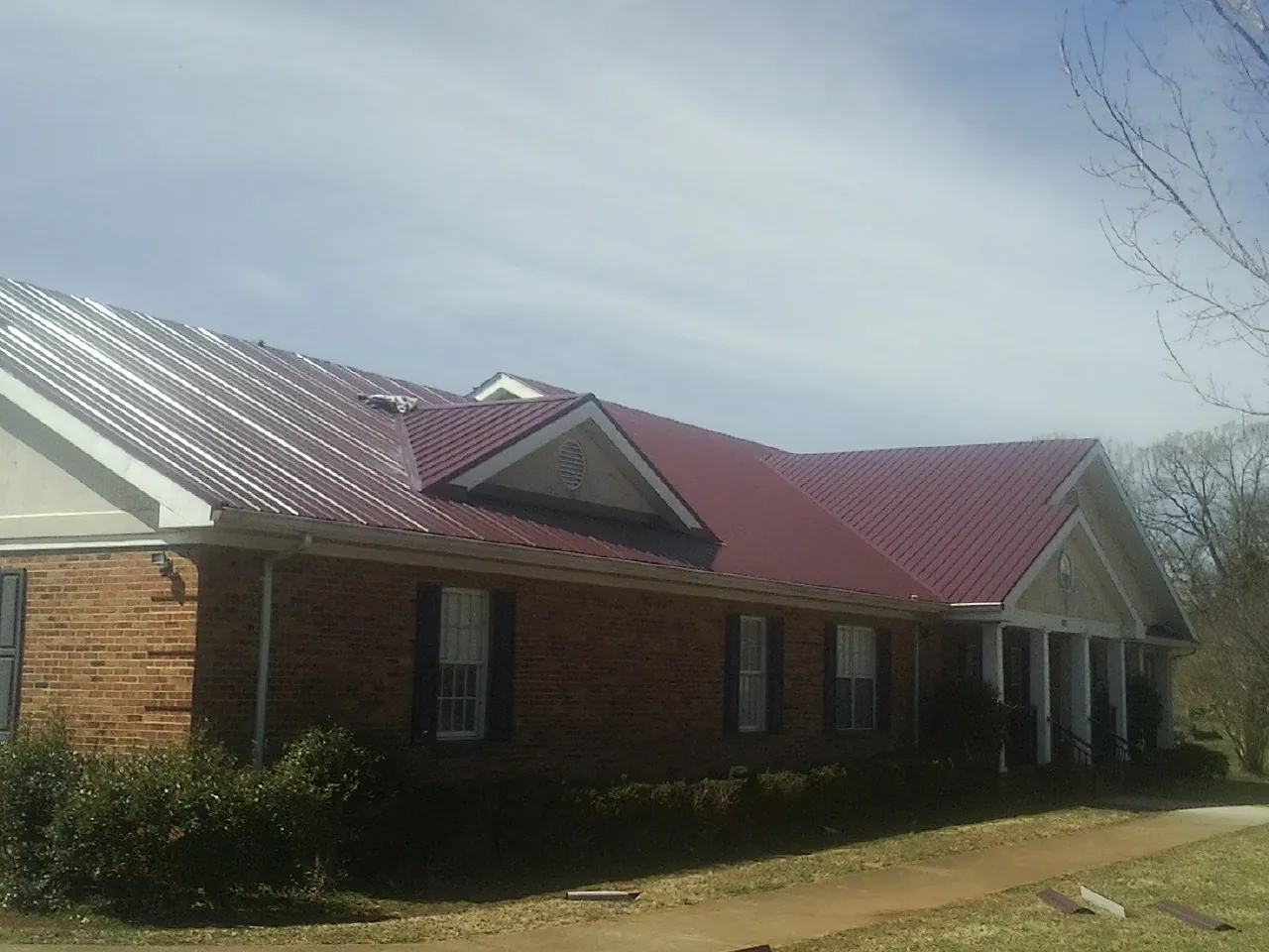 Red metal roof with gabled entries on a long brick building, from a Hail Damage Roof Repair job in Roxbury Crossing