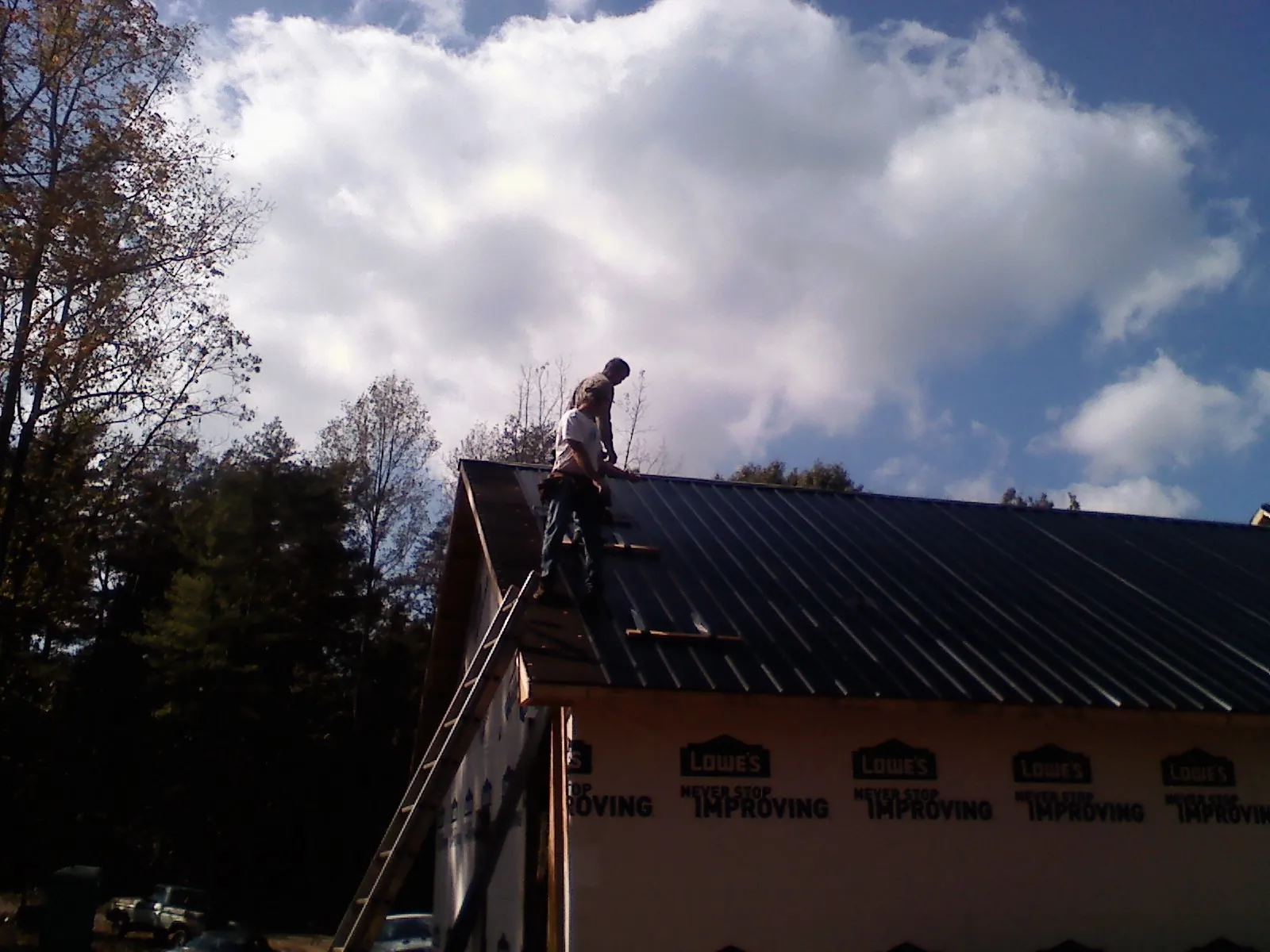 Roofer fastening dark metal panels high against a cloudy sky, from a Roof Inspection job in Roxbury Crossing