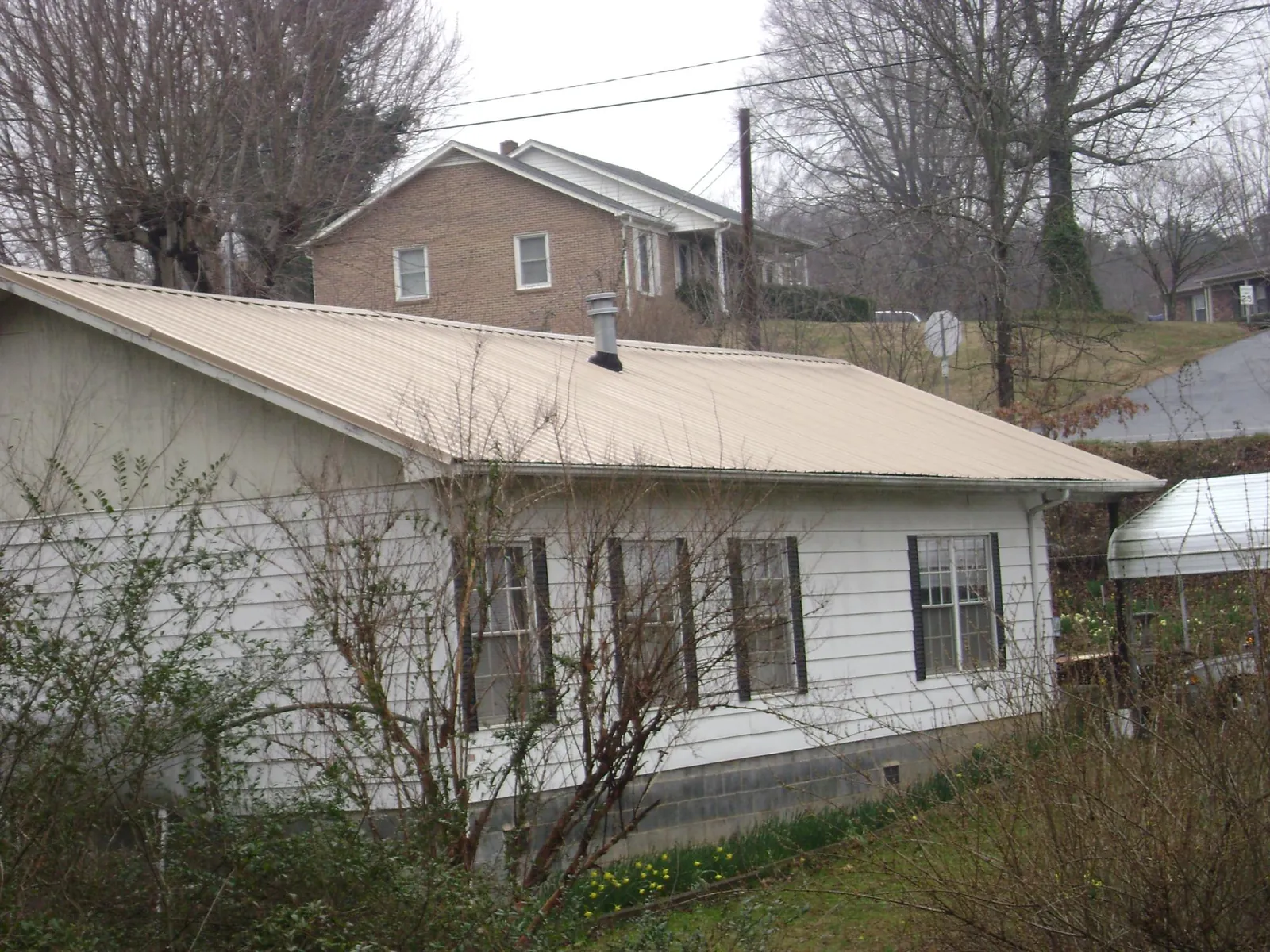 Tan metal roof on a white sided house set into a hillside — Commercial Roofing by Roofing Brothers in Roxbury Crossing