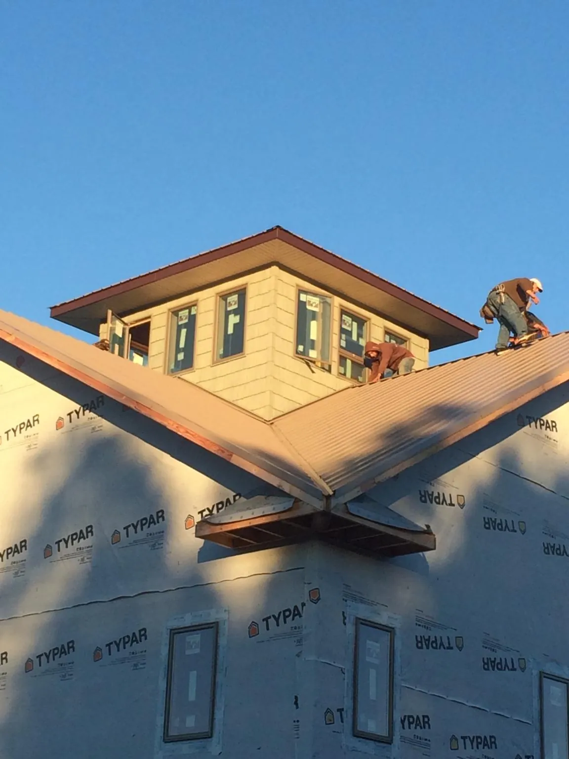 Roofers working around a rooftop cupola on a new metal roof at sunset in Roxbury Crossing